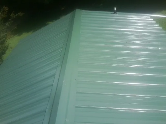 New green metal panels meeting at the ridge of a roof — Flat Roof Repair work by our crew in Cedar Grove
