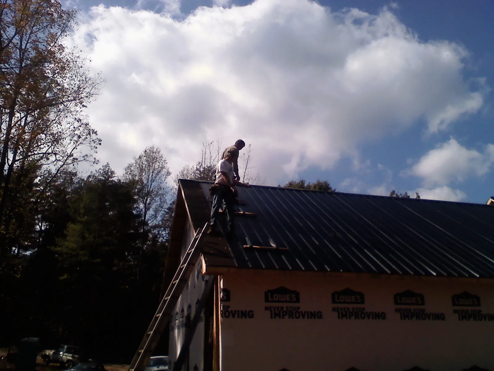 Roofer fastening dark metal panels high against a cloudy sky, from a Roof Inspection job in Cedar Grove